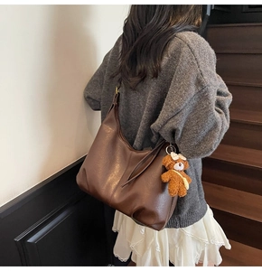 Sac hobo en cuir marron avec pendentif ours en peluche sur un escalier en bois chic