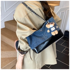 Detail of color-block denim tote bag with chain strap and teddy bear charm on model