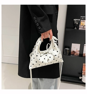 Close-up of a white polka dot dumpling bag with drawstring bow and metal bead detail