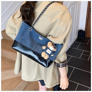 Model showing a patchwork denim tote bag with chain strap and a brown teddy bear pendant