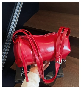 Detailansicht einer glänzenden roten Zylindertasche mit silbernen Schnallen und Gurt