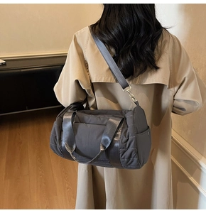 Detail of grey quilted duffle bag with detachable strap worn by model in a trench coat