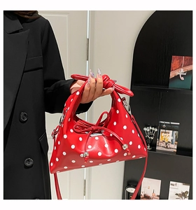 Detail of red polka dot handbag featuring knotted handle and decorative bow with metallic logo