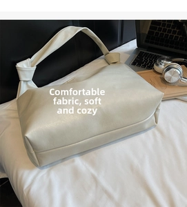 Close-up of white soft leather hobo bag with knotted strap on a bed with lifestyle props