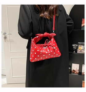 Detailed view of red polka dot handbag with bow handle and detachable strap on a model