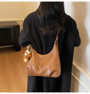 Détail d'un sac hobo demi-lune marron en cuir poli avec un joli pendentif d'ours