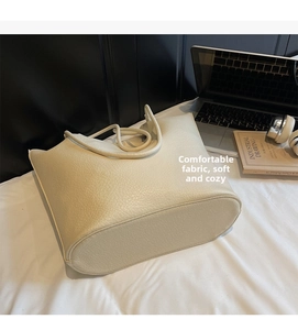 Detailed view of off-white lychee pattern leather tote bag on a cozy bed background