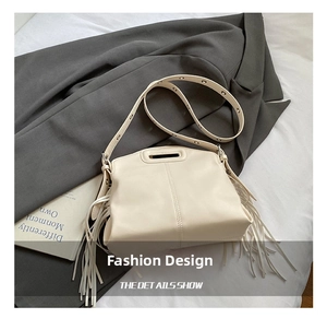 Detail of beige fringe shoulder bag with cutout handle on grey blazer background