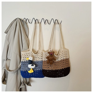 Detail of hand-woven gradient crochet tote bags with plush pendants on a wall hanger