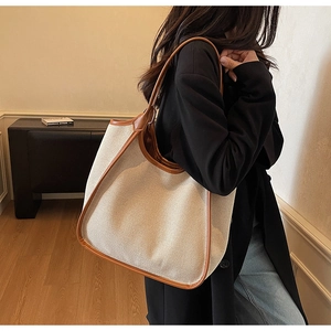 Détail d'un grand sac cabas en toile avec bordures en cuir marron porté par un mannequin