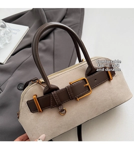 Detail of grey faux suede bag with dark brown leather handles and golden hardware accents