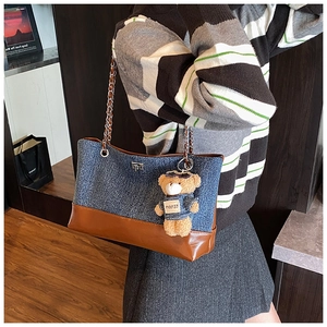 Side view of contrast color tote bag with denim fabric, leather trim and bear charm