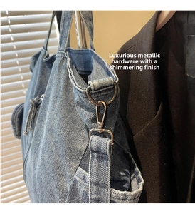 Detail of blue denim tote bag featuring shiny silver hardware hooks and a side pocket