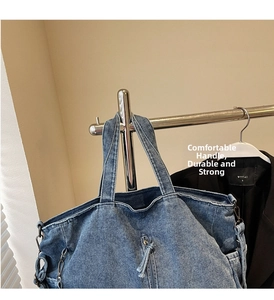 Detail of blue washed denim tote bag showing wide handle and metallic chain accents