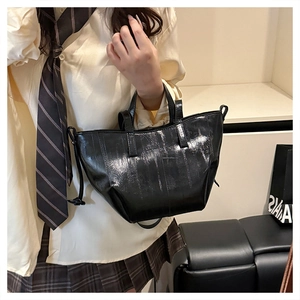 Close-up of a glossy black patent leather tote bag with elegant vertical stitching detail