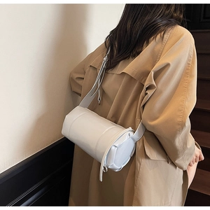 Chic ivory white cylinder pillow bag worn over a beige coat for a stylish street look