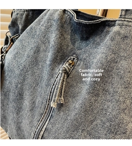Close-up of washed blue denim tote bag texture with zipper and tassel detail