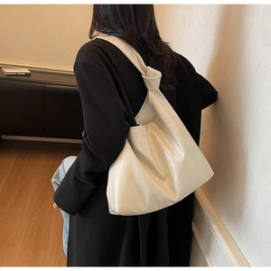 Large cream-colored soft leather tote bag with unique knot detail on the shoulder strap
