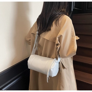 Back view of light grey glossy leather cylindrical pillow bag on khaki trench coat