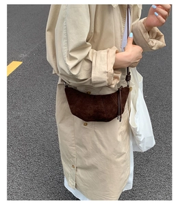 Détail d'un sac croissant en daim marron foncé avec coutures plissées sur un trench beige