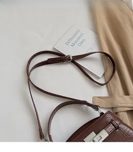 Detail of dark brown crocodile textured handbag featuring silver lock and adjustable strap