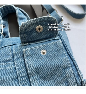 Detail of light blue denim bag featuring contrast stitching and silver metal snap button