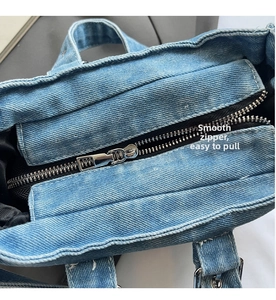 Detail of blue denim tote bag featuring a smooth silver metal zipper and black lining