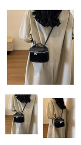 Detail of a black pebbled leather vanity bag with silver zipper and slim crossbody strap