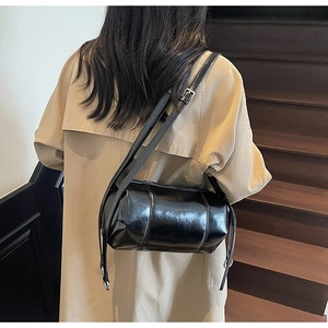 Detail of a black glossy cylinder crossbody bag with stitching on a vintage staircase