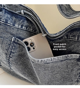 Detail of the front pocket on washed denim crossbody bag holding a smartphone