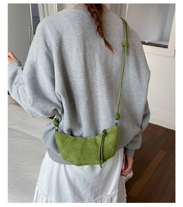 Sac croissant en daim vert porté par un mannequin dans un intérieur chaleureux