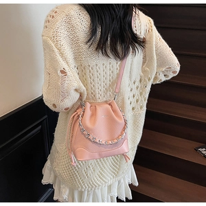 Detailed side view of a pink drawstring bucket bag with silver chain and mesh texture