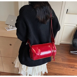 Detailed view of a glossy red cylinder shoulder bag worn over the shoulder by a model