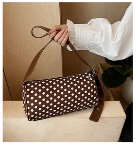 Close-up of a stylish polka dot barrel bag with brown leather strap and silver metal hardware