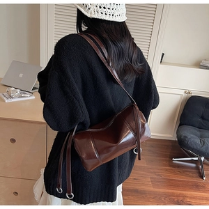 Detail of dark brown glossy cylinder bag with metal ring buckle on a shoulder strap