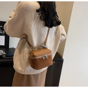 Close-up of a brown suede and leather vanity bag featuring silver zippers and hardware
