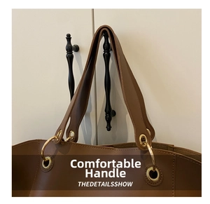 Detail of wide brown tote handle with golden metal rings and reinforced stitching