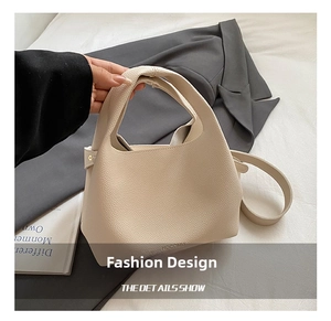 Detail showing beige lychee grain leather texture and dual-handle design of bucket bag