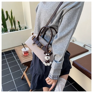 Detailed view of beige canvas shell bag with brown leather trim and a cute dog charm