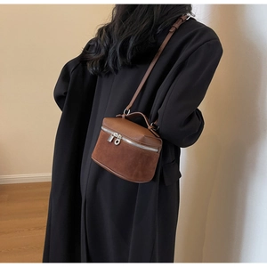 Detail of vintage brown textured leather crossbody bag with silver zipper on black coat