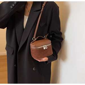 Detail of a brown leather and suede vanity crossbody bag on a model wearing a black coat