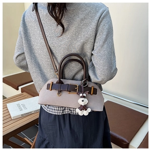 Detail of grey suede shell bag with dark brown leather handles and puppy charm