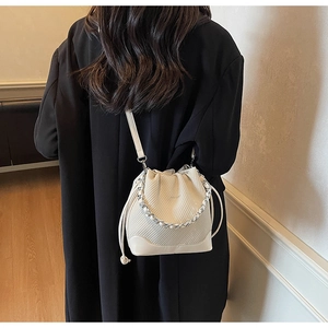Detail of cream drawstring bucket bag with geometric texture and silver chain on model