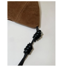 Close-up of brown suede bag featuring black knotted shoulder strap and fine stitching