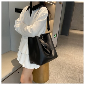 Modern black matte leather bucket tote bag shown from side angle on a model