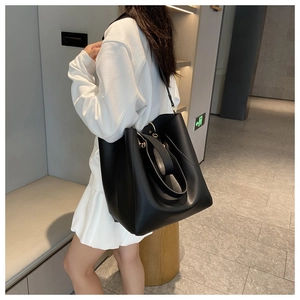 Side view of large black tote bag with double straps worn by model in minimalist setting