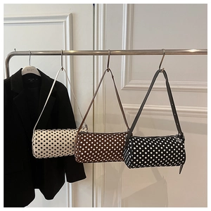 Detailed view of three polka dot cylinder bags hanging in beige, brown, and black colors