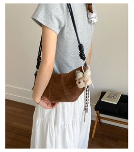 Detail of brown suede croissant bag with decorative knots and a plush bear charm