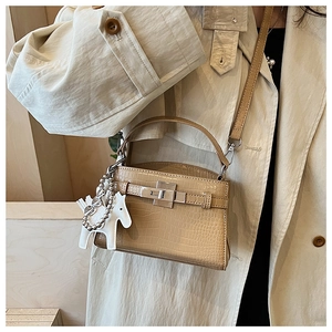Detail of beige crocodile embossed handbag with silver metal lock and leather horse charm