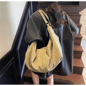 Detail of light khaki pleated bag showing textured fabric and wide shoulder strap
